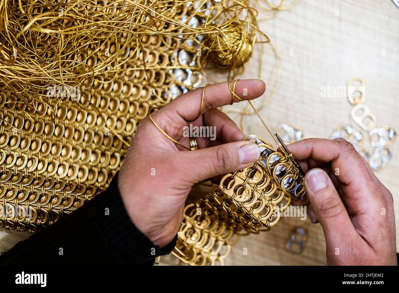 Da sopra di raccolto anonimo talentuoso persona che crocheting la posta della catena con tiri dorati dell'anello di alluminio mentre lavora in officina leggera Foto Stock