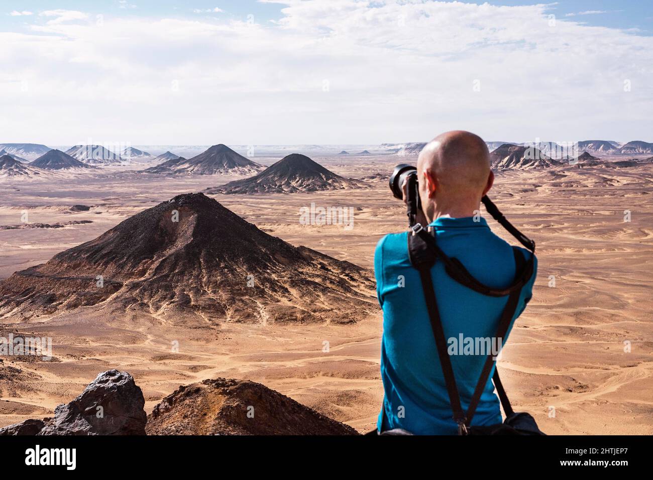 Vista posteriore di un fotografo maschile irriconoscibile che scatta foto con una fotocamera professionale di tumuli situati nel deserto nero durante il viaggio in Egitto Foto Stock