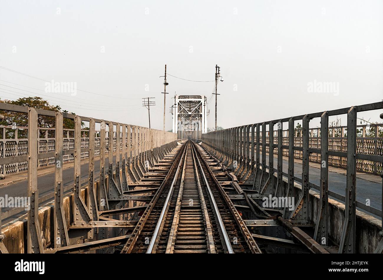 Lunghe rotaie in metallo dritte vuote con barriere contro il cielo limpido e senza nuvole su strada con linee elettriche il giorno d'estate Foto Stock