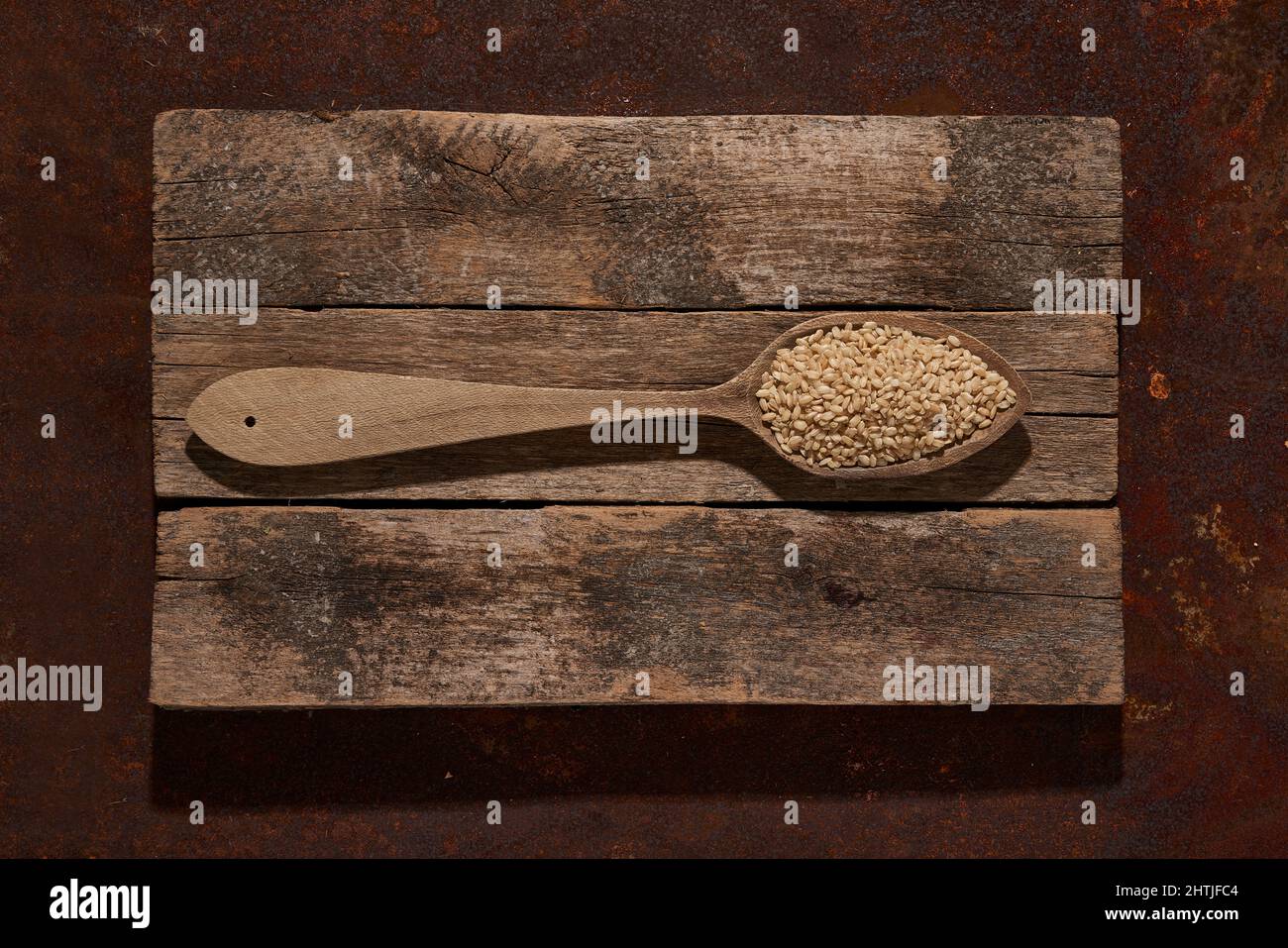 Cucchiaio di legno con vista dall'alto e semi di sesamo crudo su assi di legno posti sul tavolo in camera luminosa Foto Stock