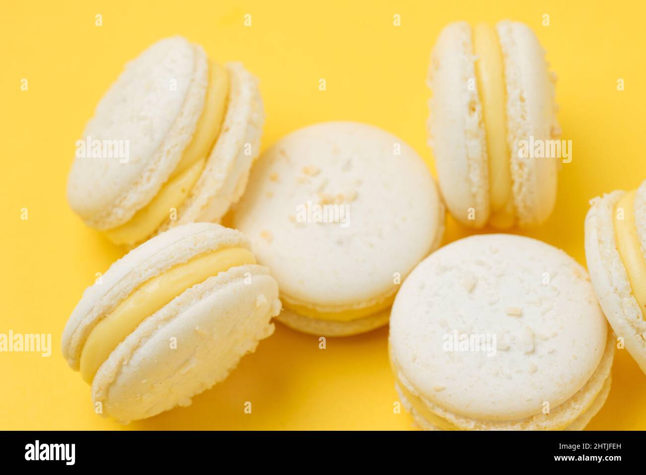 Un mucchio di macaron dolci alla vaniglia con gustoso ripieno giallo servito su sfondo giallo in camera luminosa Foto Stock