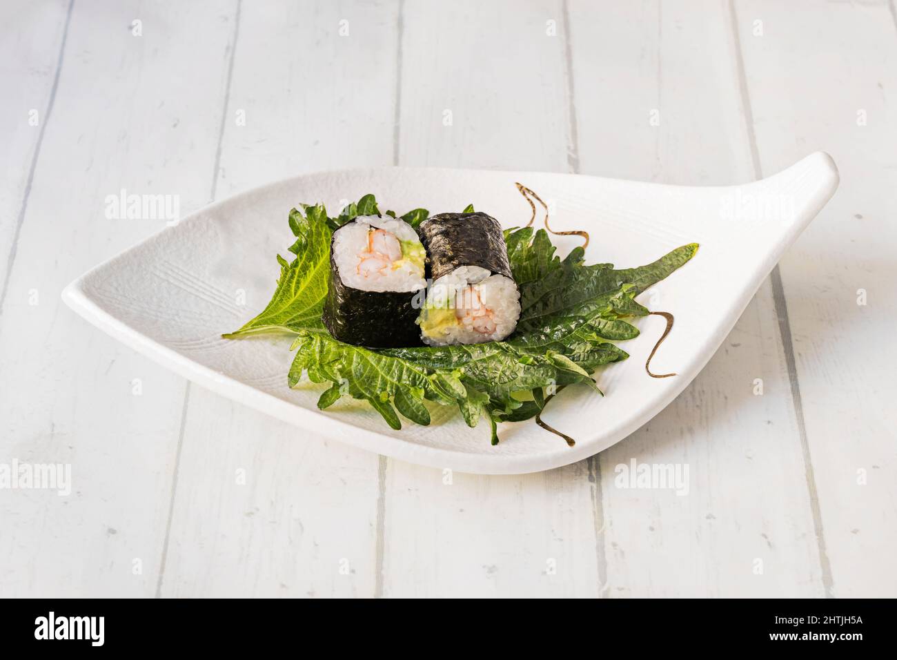 Due pezzi di gamberi e di avocado maki arrotolati con alghe nori, riso bianco giapponese su una foglia di shiso Foto Stock