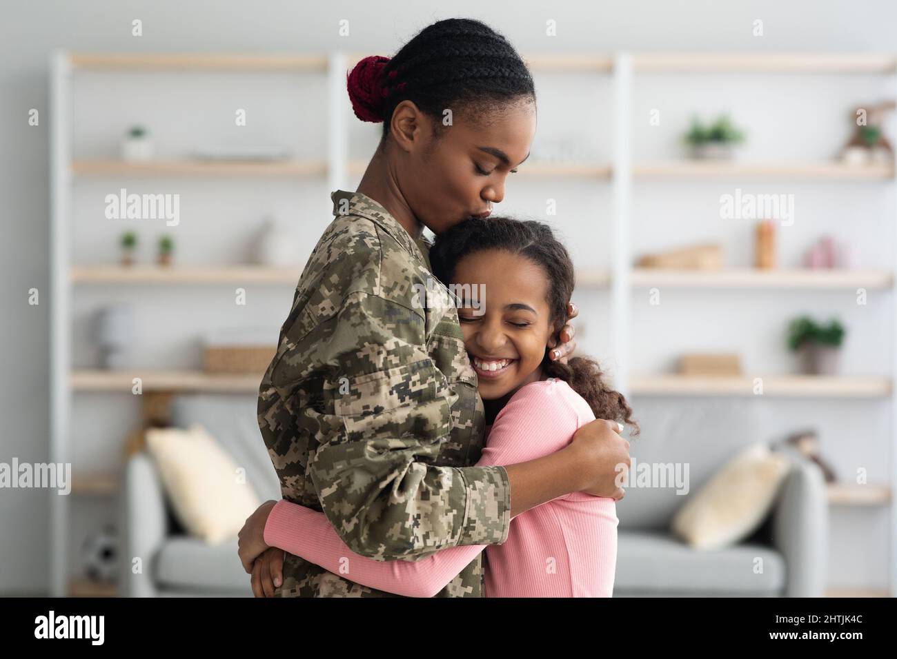 Vista laterale della madre nera in uniforme militare abbraccia il bambino Foto Stock