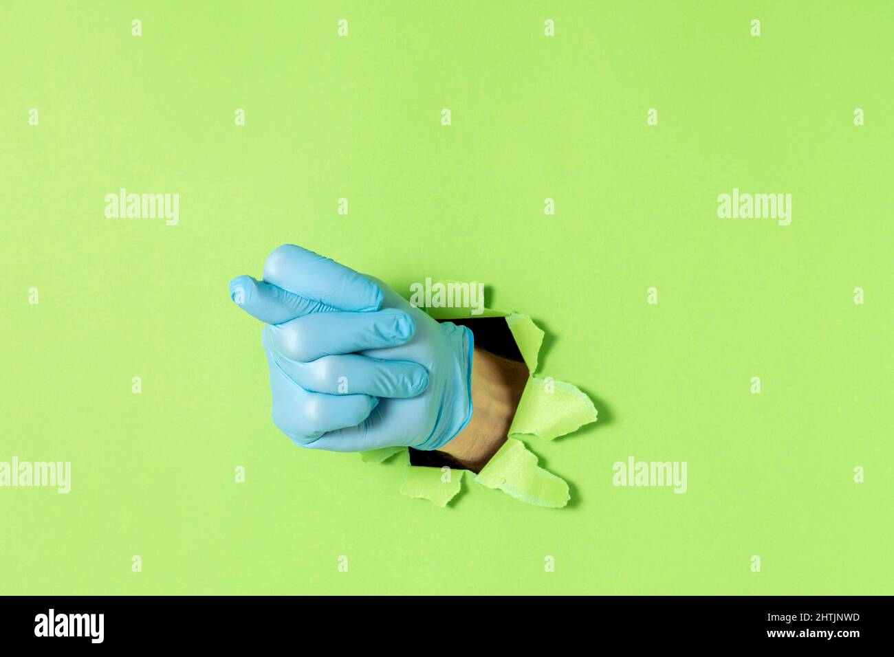 Figura come gesto della mano, che denota umiliazione o negazione. La mano maschio in un guanto in lattice blu sporge da un foro strappato in carta verde. Spazio di copia. Foto Stock
