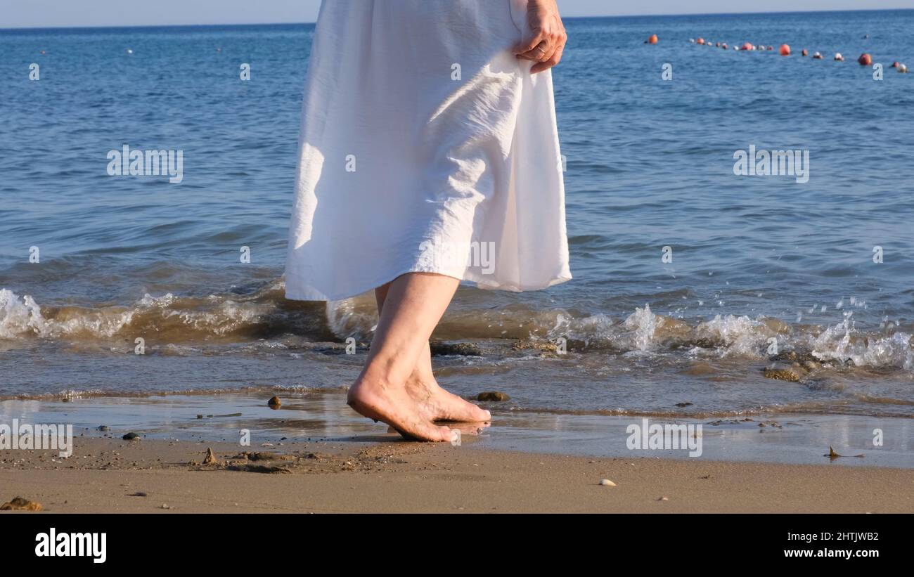 le gambe mature delle donne camminano lungo la spiaggia sabbiosa e si  tuffano in mare in