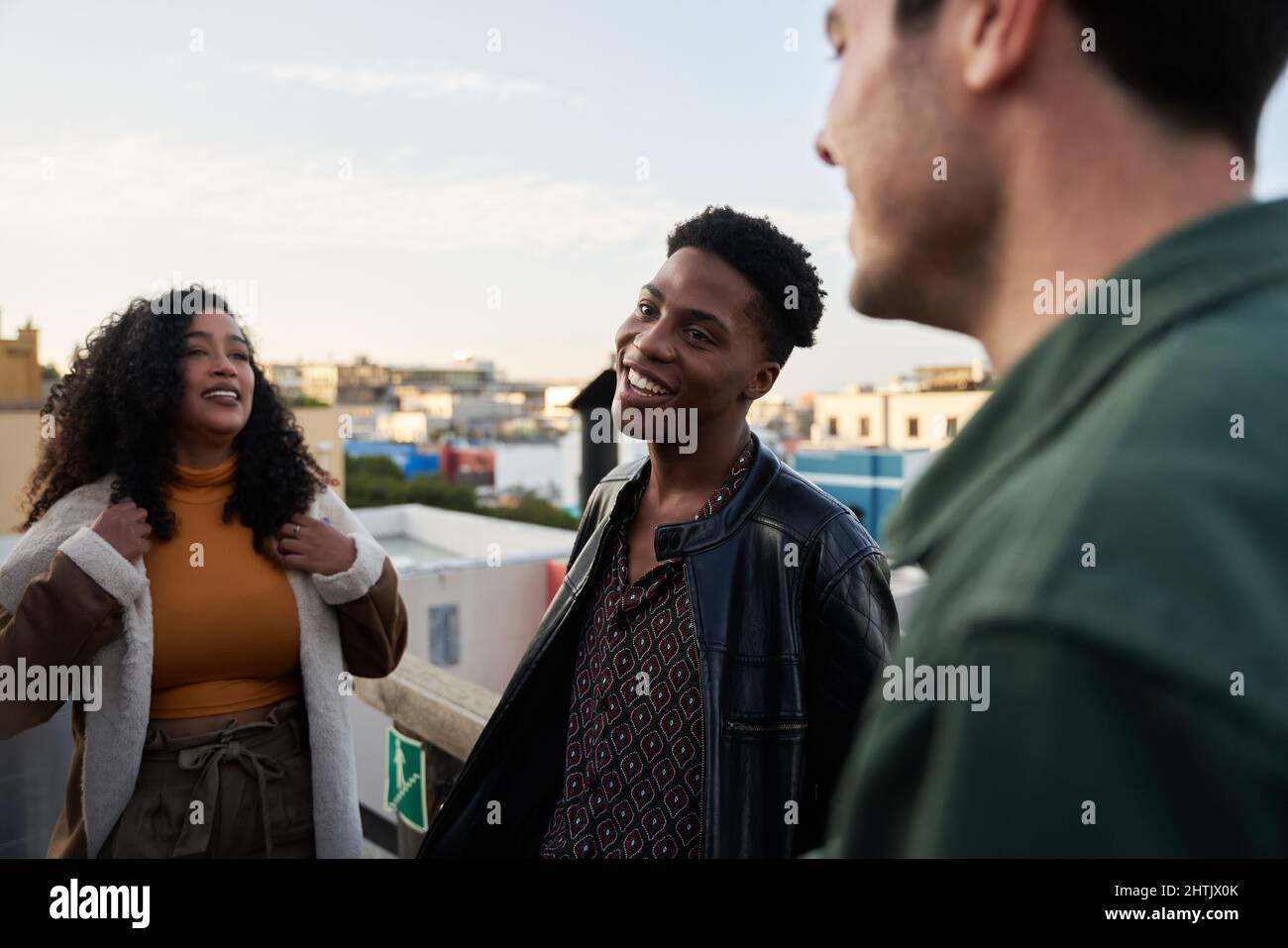 Giovane uomo nero adulto sorridente mentre tra amici multiculturali in città su una terrazza sul tetto. Foto Stock