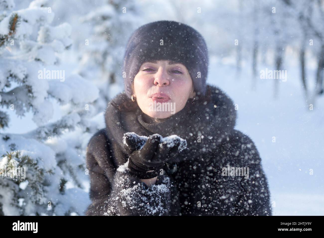 Una donna adulta di 40 anni in un parco invernale in un cappotto e cappello  di pelliccia mink soffia la neve fuori dal palmo Foto stock - Alamy