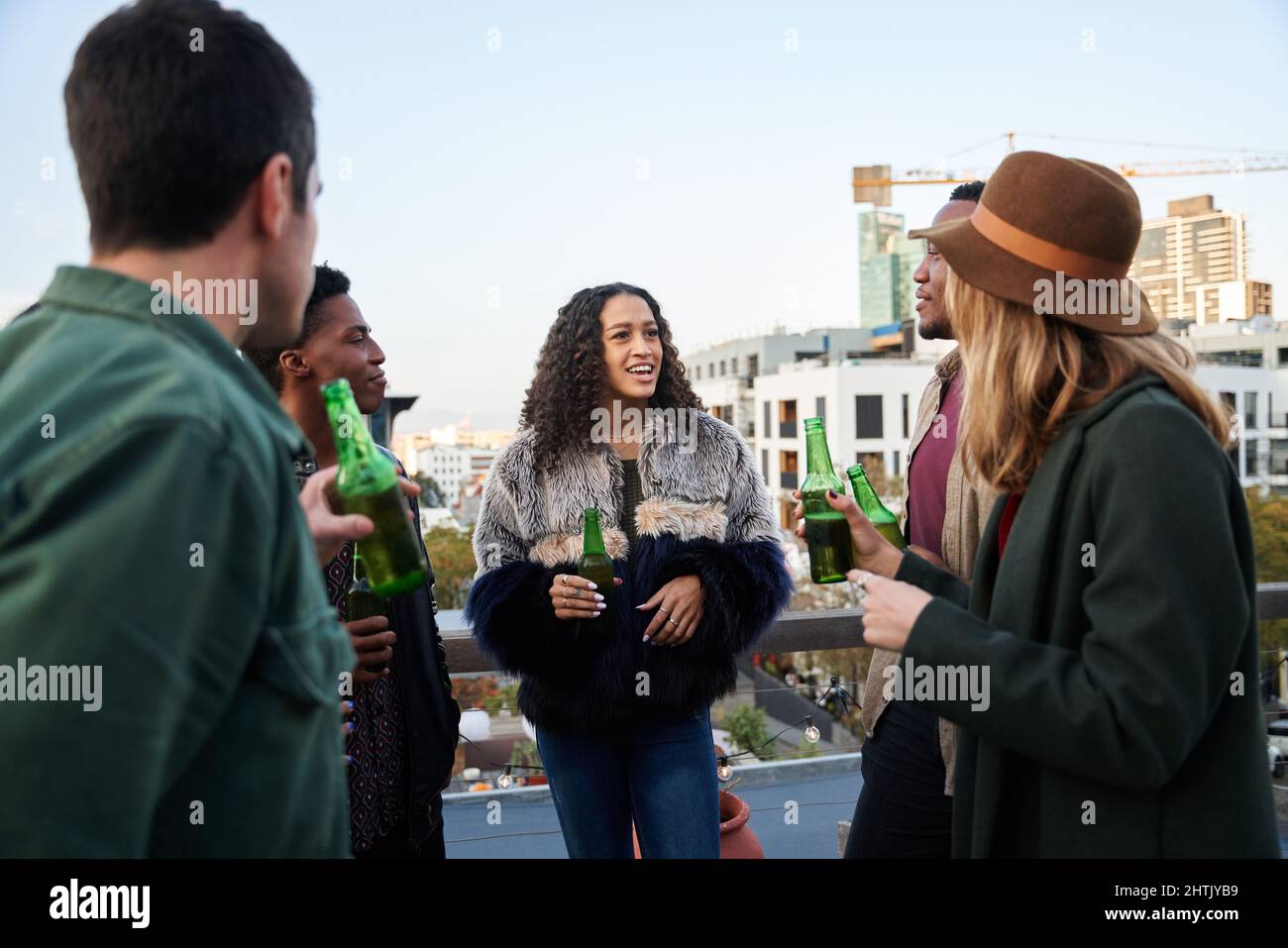 Gruppo multiculturale di giovani adulti che chiacchierano con bevande sul balcone di una terrazza panoramica della città. Foto Stock