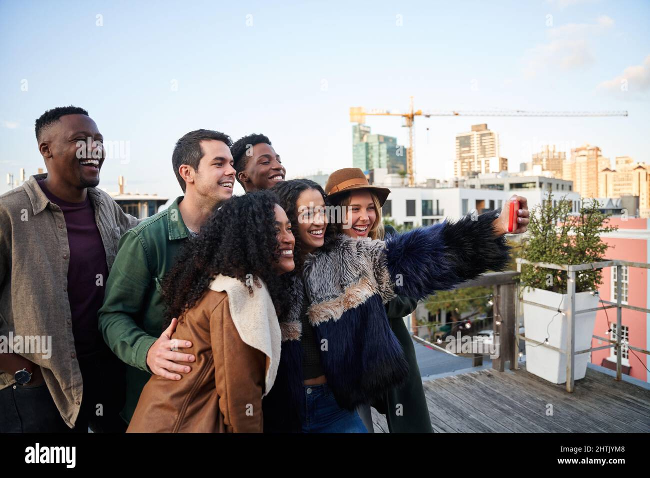 Gruppo multiculturale di amici che prendono un selfie in una festa sul tetto. Sorridente con sfondo urbano. Foto Stock