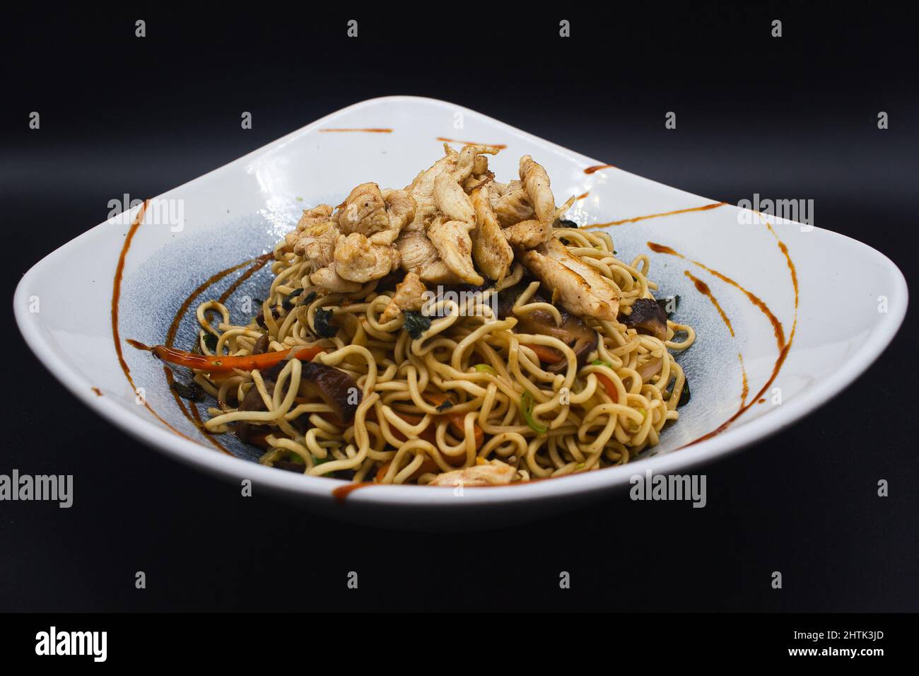 Yakisoba di pollo cotto, tagliatelle di wok asiatico con pollo, sesamo, salsa teriyaki e verdure pronte da mangiare. Foto studio con sfondo nero. Foto Stock