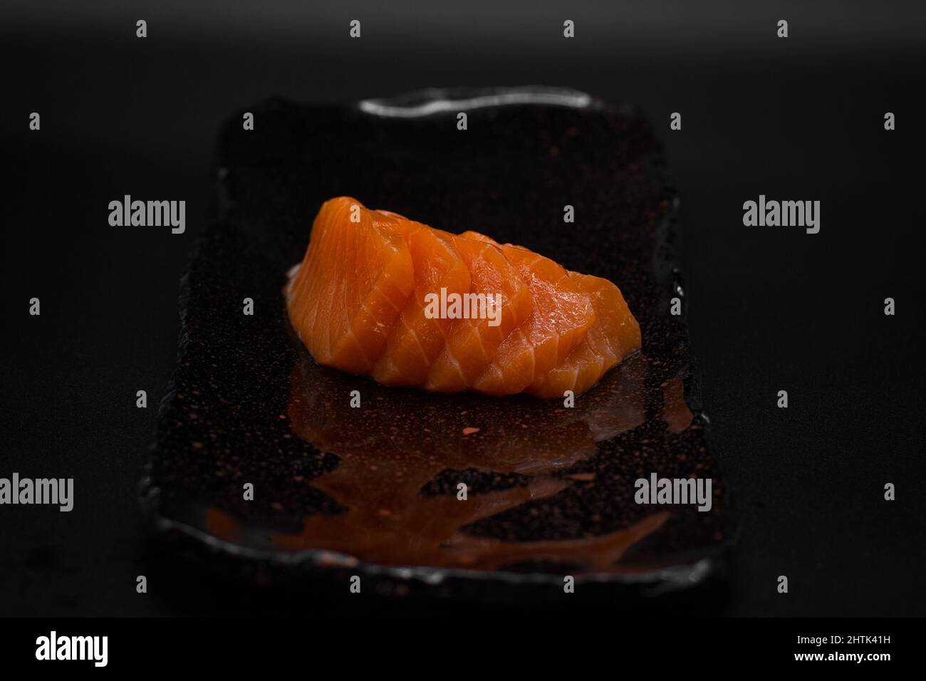 Tradizionale Sashimi giapponese tagliato, salmone selvatico crudo e fresco dalla Norvegia affettato e servito in piatto nero con sfondo nero in modo minimalista. Foto Stock