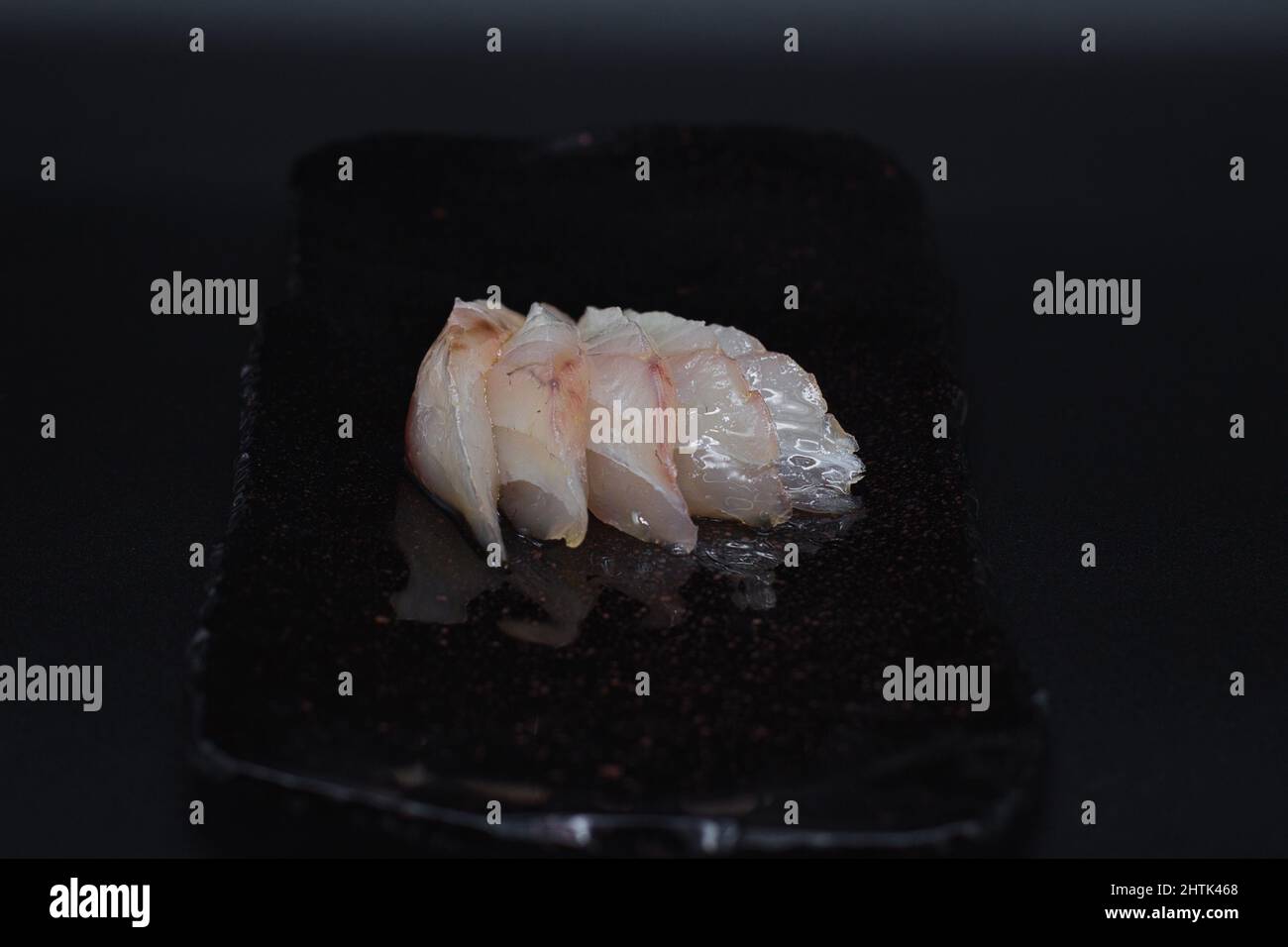 Tradizionale Sashimi giapponese tagliato, crudo e pesce bianco fresco affettato e servito in piatto nero con sfondo nero in modo minimalista. Foto Stock