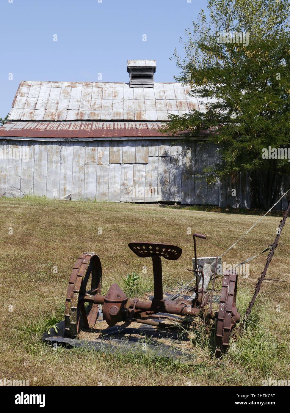 Arrugginito vecchio impianto agricolo in un campo con un vecchio fienile Foto Stock