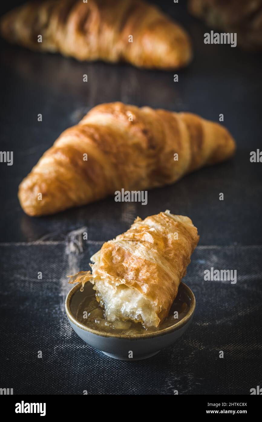 Pezzo di delizioso croissant francese immerso nella marmellata, sfondo nero, verticale Foto Stock