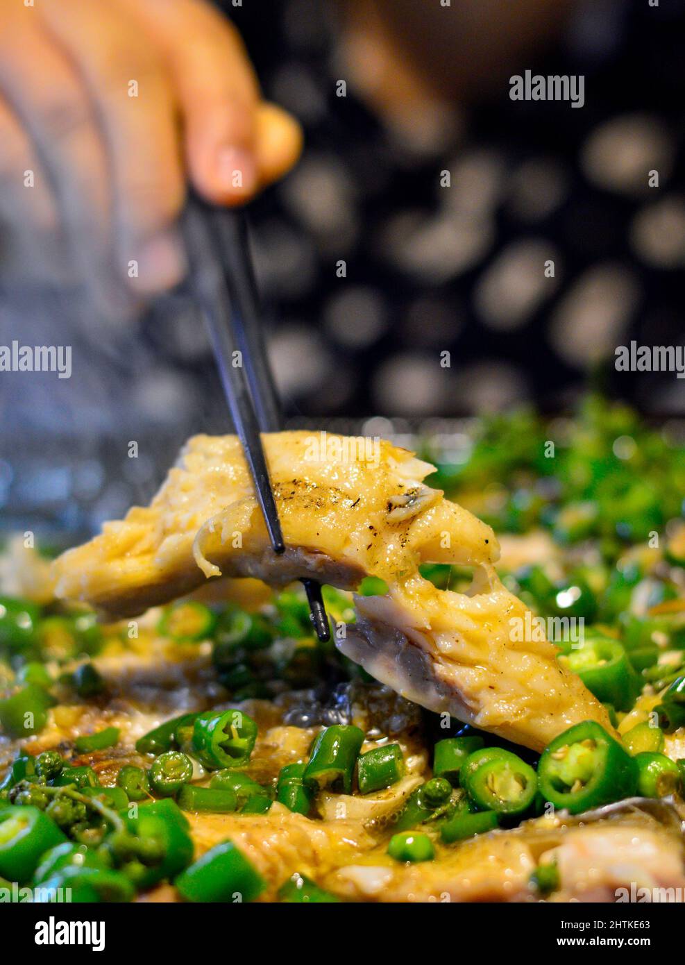 Chopsticks raccogliere il pesce da un hot pot cinese con peperoncini verdi. Foto Stock