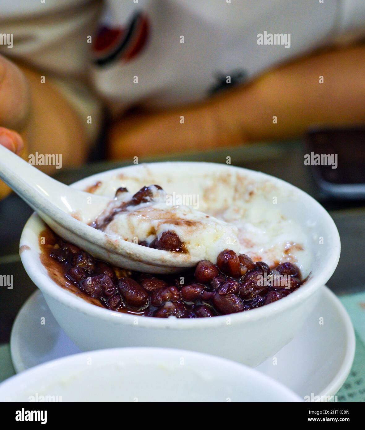 Cucchiai a mano il budino di latte a doppia pelle di fagiolo rosso da un recipiente bianco. Il budino di latte a doppia pelle è un dessert popolare a Hong Kong. Foto Stock