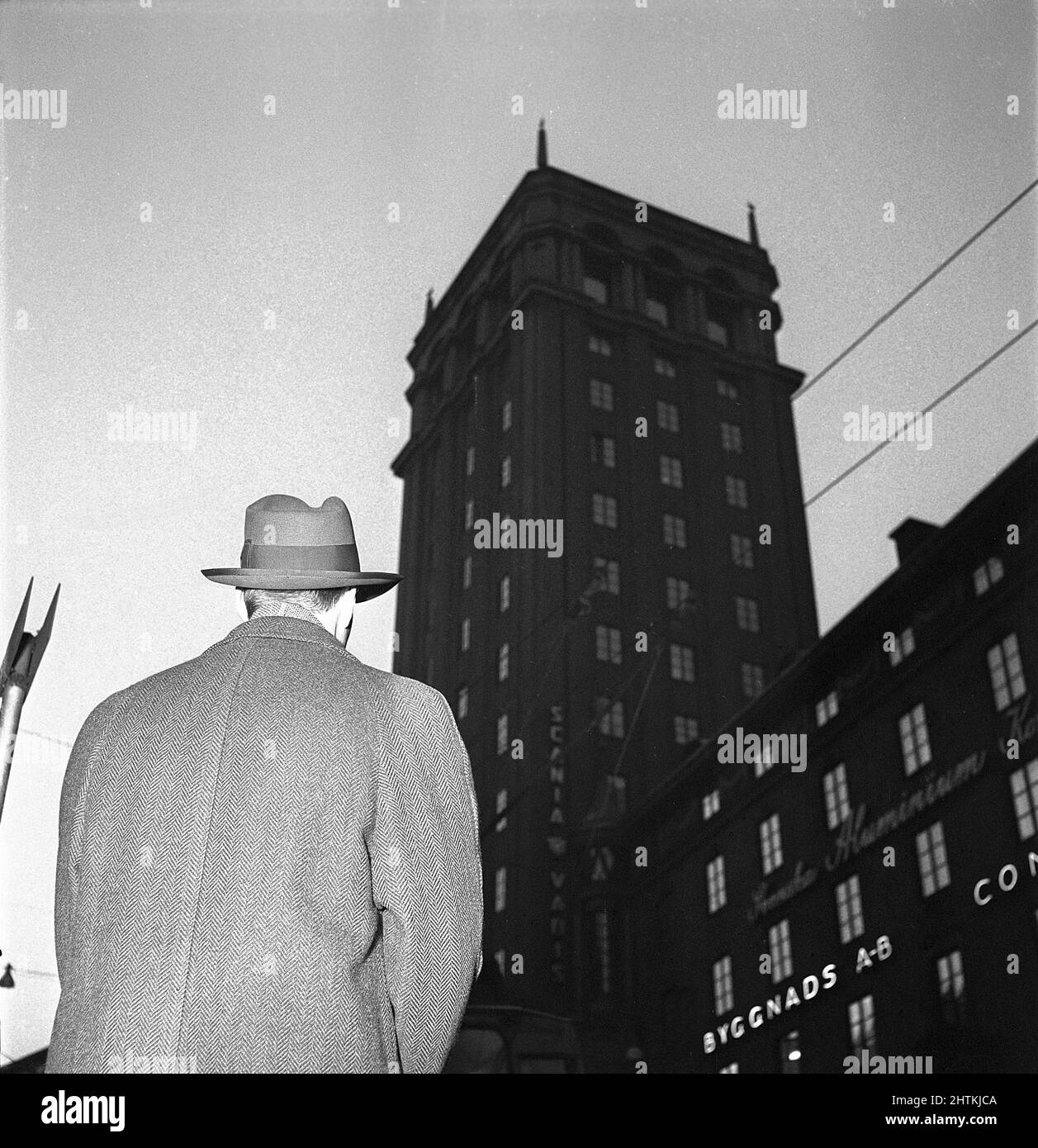 Nel 1950s. Un uomo in un cappotto e cappello è raffigurato nella strada dal basso con la silhouette di un alto edificio sullo sfondo. Svezia 1951 Kristoffersson Ref BE86-5 Foto Stock