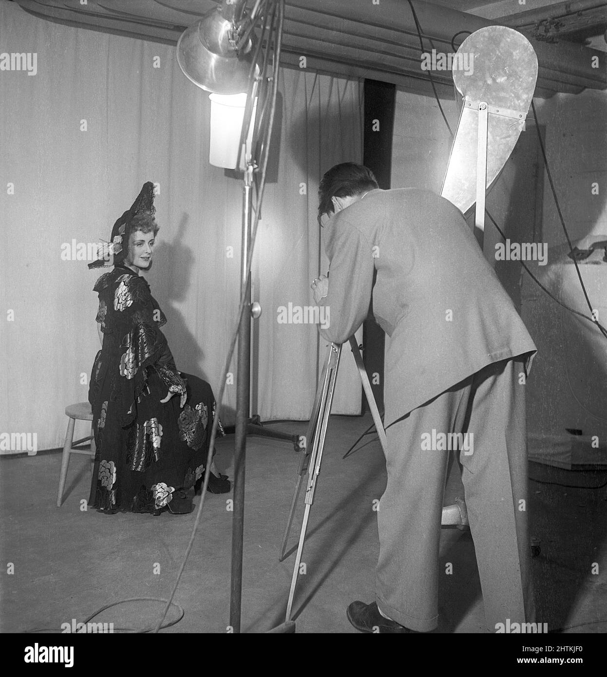 1950s fotografo e modella di moda. Una giovane donna in uno studio di fotografi e la fotografa si concentrano su di lei con la sua macchina fotografica. Le luci e lo sfondo sono disposti in modo da scattare la migliore foto possibile. Svezia 1951 Kristoffersson Ref BE14-8 Foto Stock