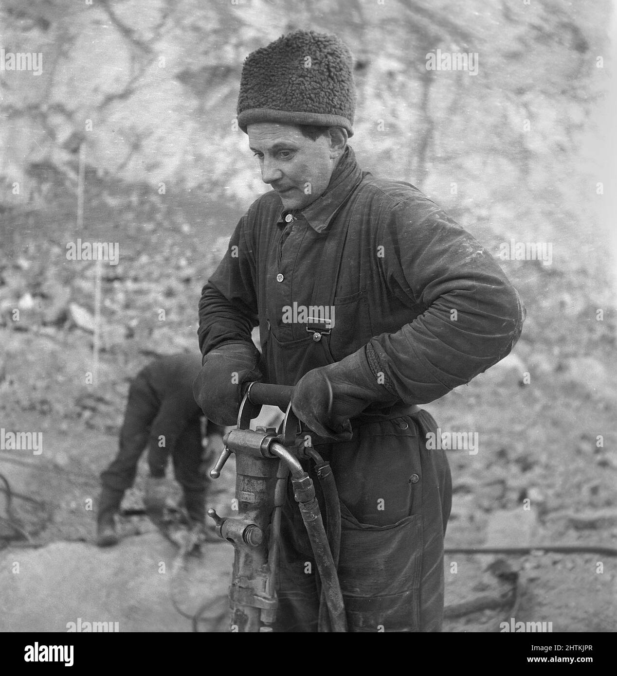Kiruna Svezia nel 1950s. La miniera aperta e i lavoratori che perforano fori per mettere esplosivi in. Il trapano è alimentato da aria compressa e il rumore sarebbe stato molto alto, ma l'uomo che lavora con esso sembra non notare il suono anche senza indossare alcuna protezione per le orecchie. Potrebbe già avere un'audizione così brutta che il problema del rumore alto non è un problema. Svezia 1954 Kristoffersson BP22-11 Foto Stock