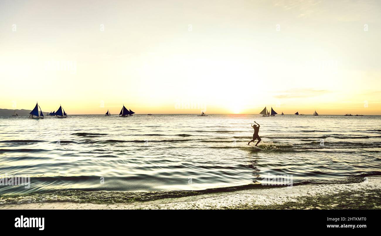 Silhouette di skimboarder al tramonto con barche a vela tipiche dell'isola di Boracay - Extreme sport e concetto esclusivo di viaggio nelle Filippine - Warm su Foto Stock