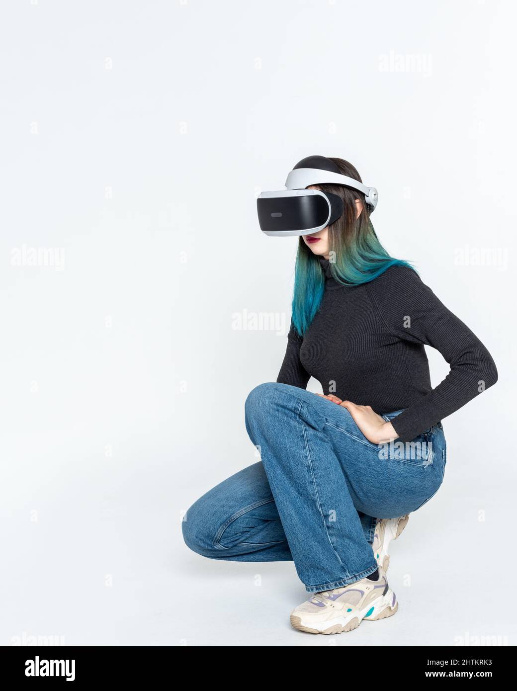 Una ragazza adolescente in un casco vr gioca nell'universo virtuale isolato su sfondo bianco, cornice verticale. Il concetto dell'universo virtuale. Vita Foto Stock