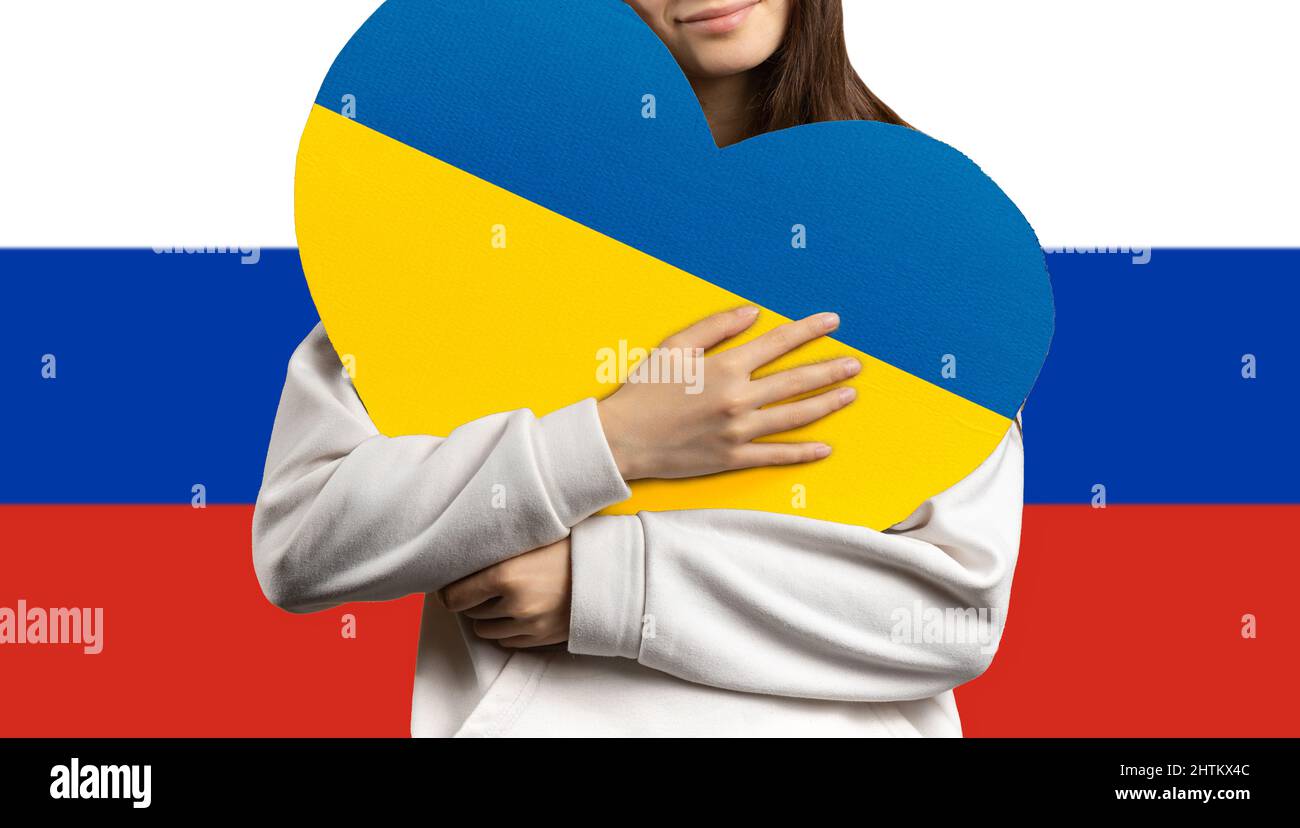 Una ragazza tiene un cuore al petto con la bandiera dell'Ucraina, e dietro di lei la bandiera della Federazione russa. Foto Stock