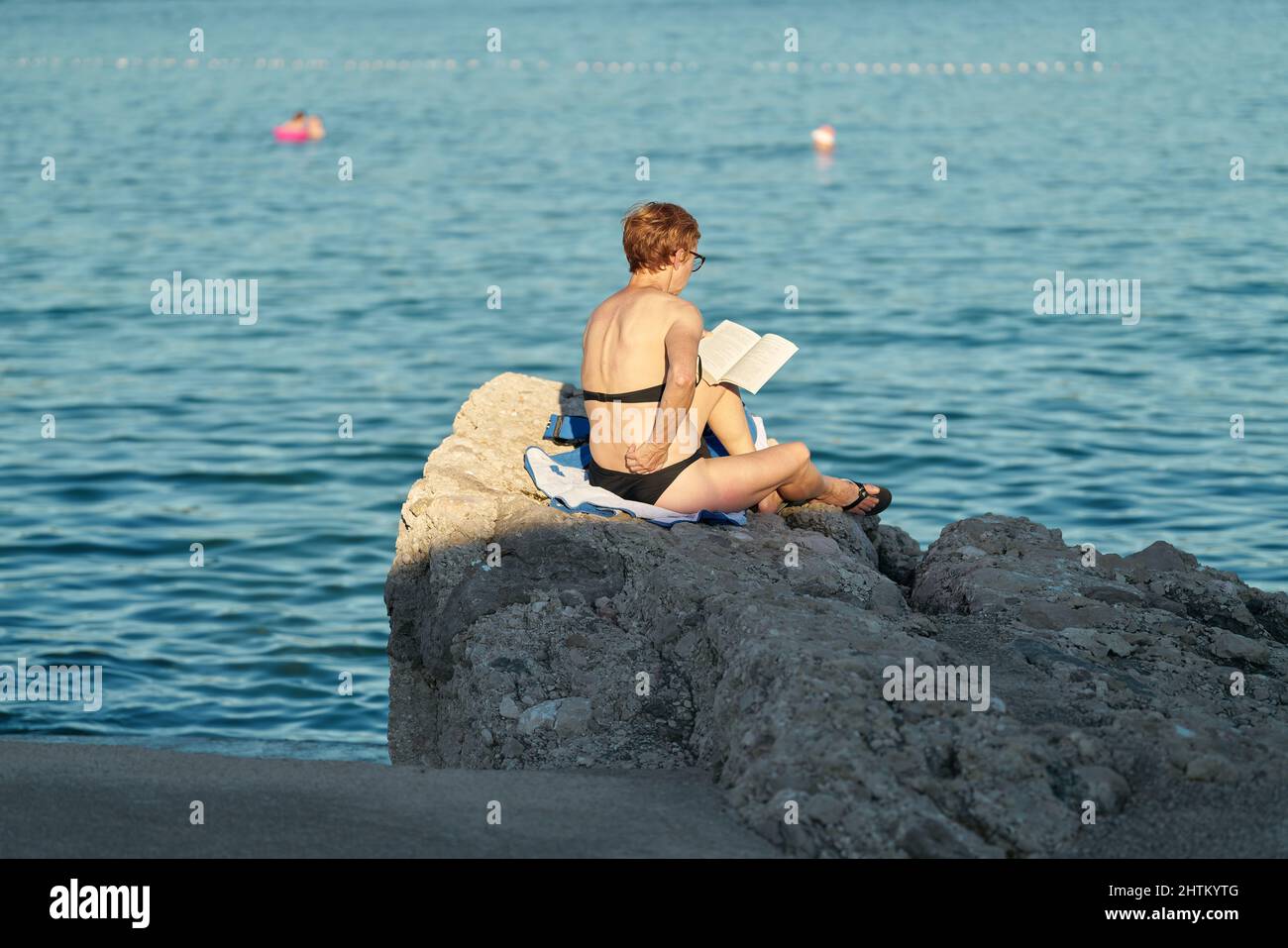 Una donna si siede vicino a Krk sulla costa dell'Adriatico croato e legge un libro Foto Stock