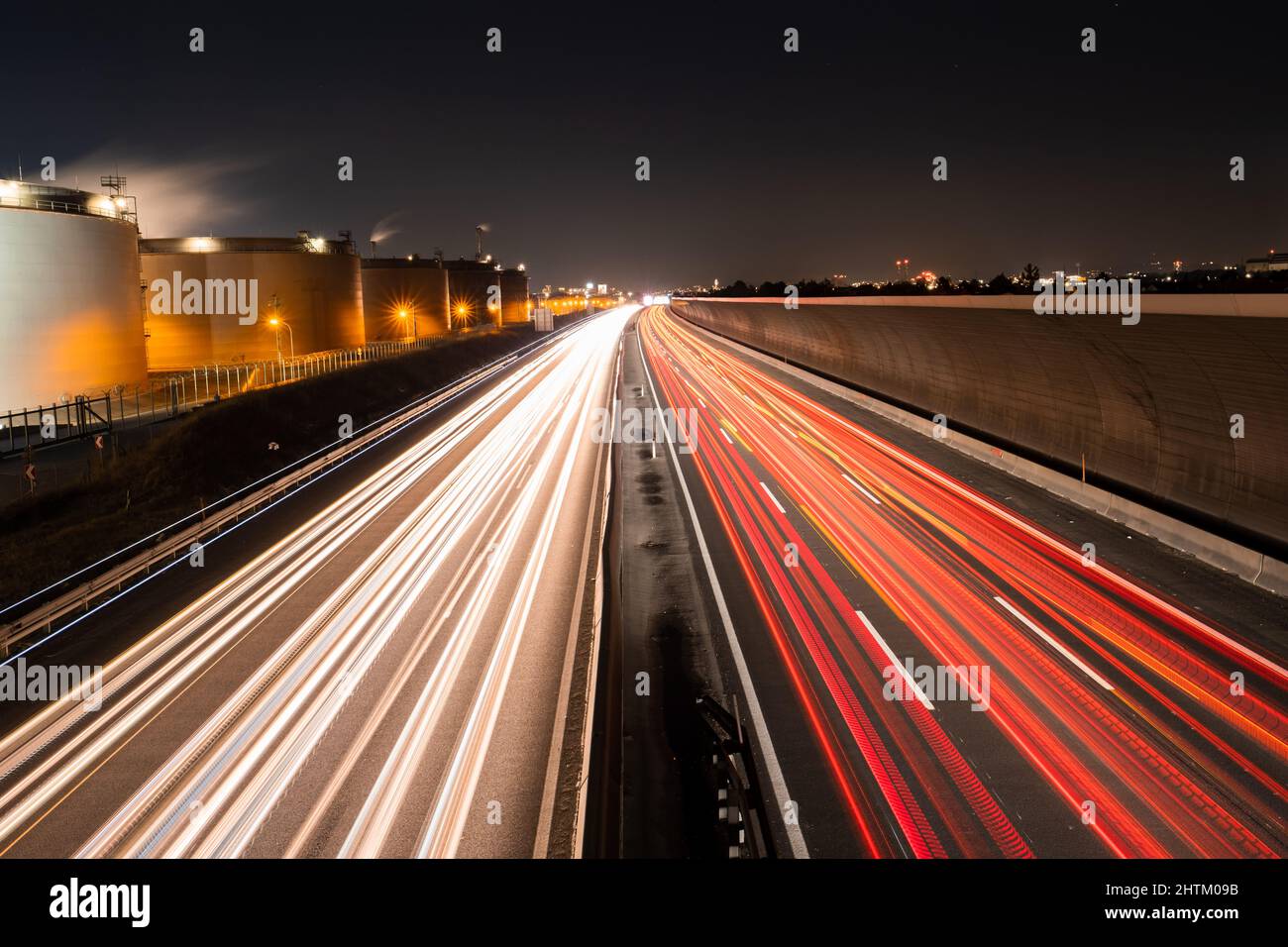 Percorsi leggeri di traffico auto su un'autostrada vicino a edifici industriali e una barriera di rumore di notte, cartolina calender idea concetto Foto Stock