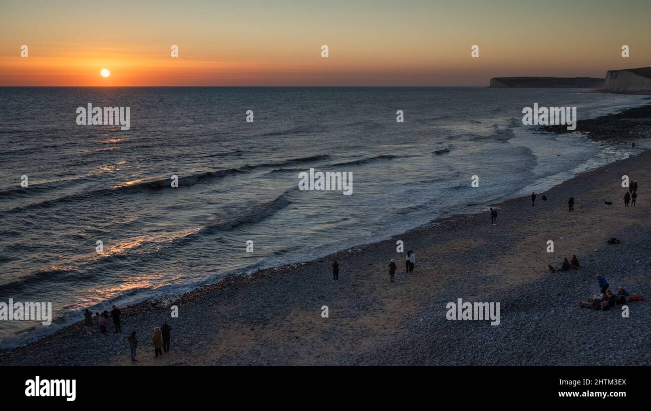 Le persone si riuniscono sulla spiaggia a Birling Gap vicino alle scogliere di Seven Sisters nel Sussex orientale, Regno Unito, per guardare il tramonto. Foto Stock