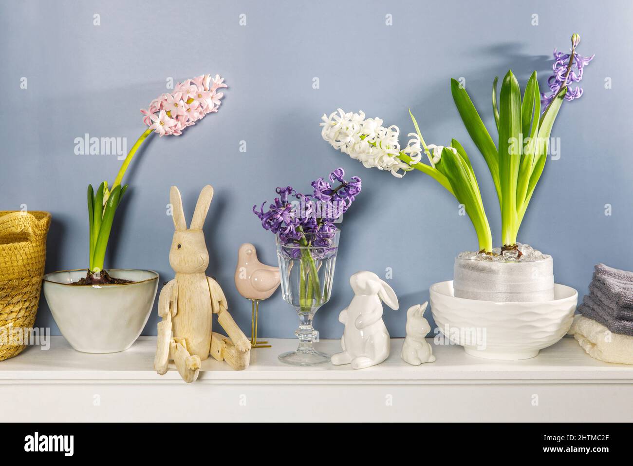 Giacinto bianco in una grande ciotola di porcellana, figurine di lepri e un uccello, sono sul camino contro la parete blu scuro. Layout. Concetto di primavera Foto Stock