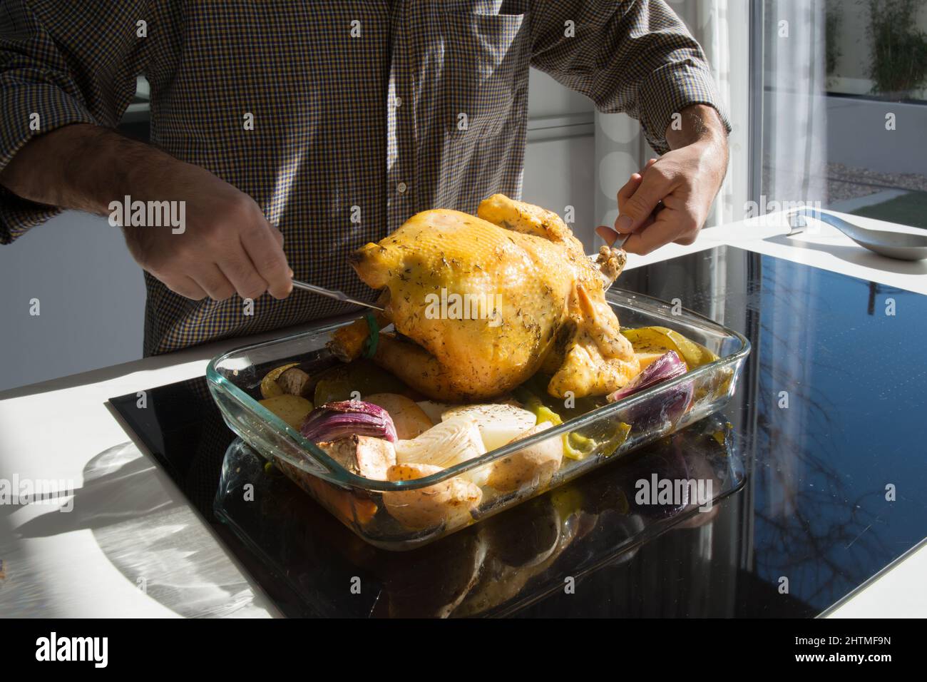 Uomo irriconoscibile che prepara un succosa pollo al forno con verdure. Cucina soleggiata. Foto Stock