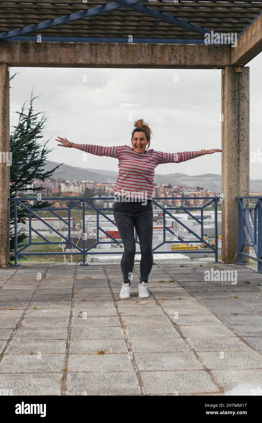 giovane bella ragazza caucasica con capelli castani che salta per strada guardando la macchina fotografica sorridente - spensierato, giovane, concetto di freschezza - vestito in nero j Foto Stock