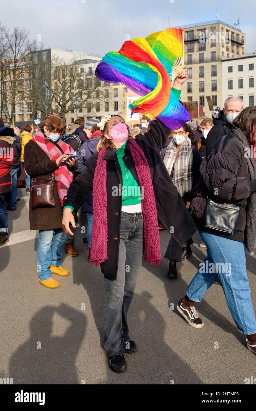Donna in maschera facciale con bandiera arcobaleno, simbolo di pace. Le persone con bandiere e cartelli ucraini protestano contro la guerra in Ucraina Foto Stock