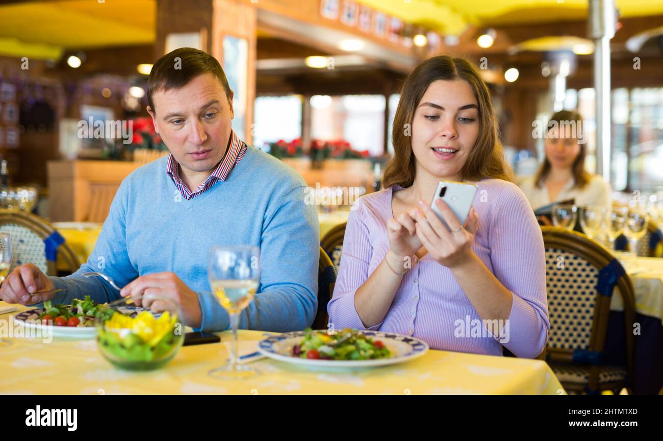 Donna che usa lo smartphone al ristorante durante la cena con il marito Foto Stock