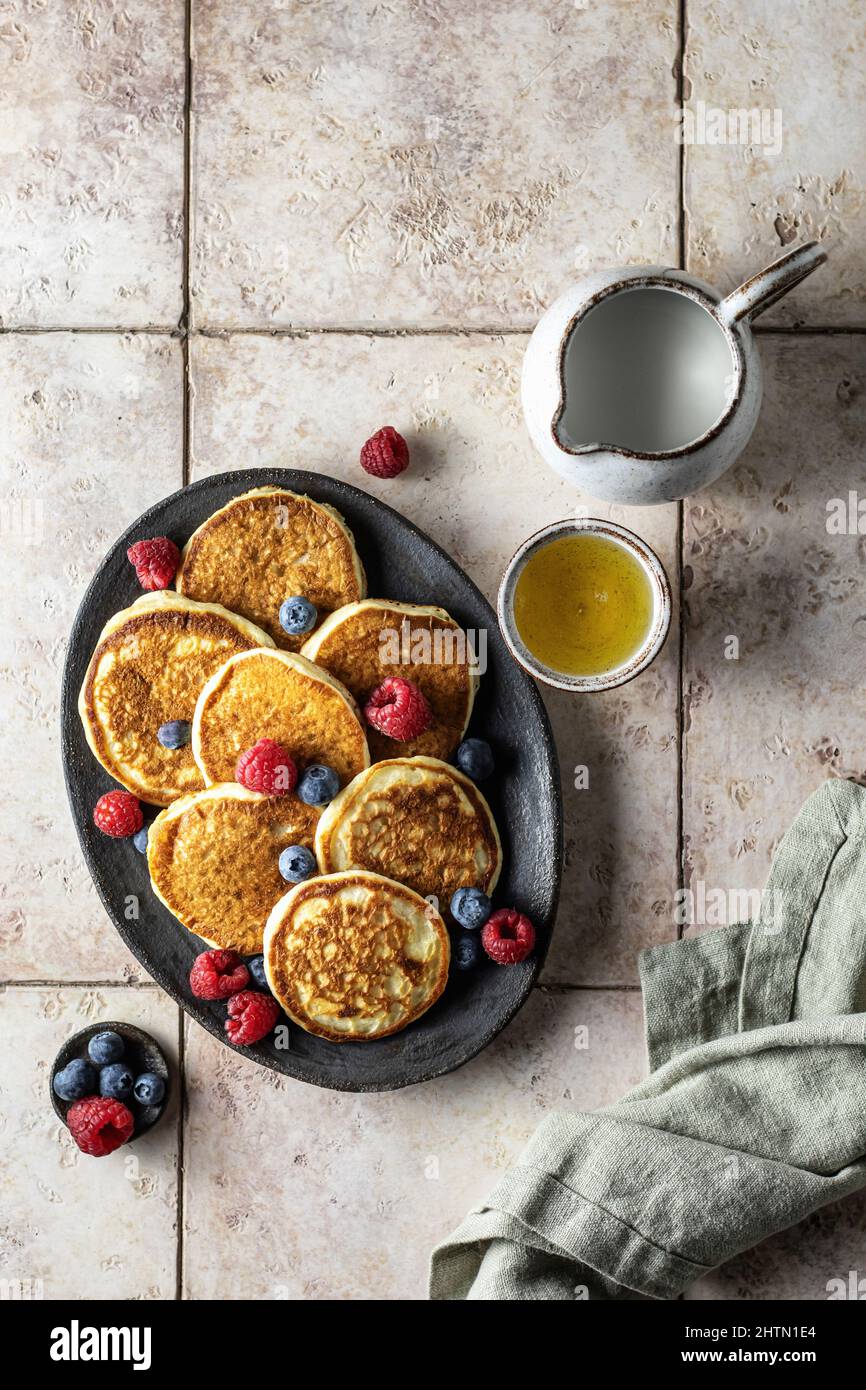 Pancake in piastra di ceramica con lamponi, mirtilli, miele e tovagliolo di lino su sfondo di piastrelle rosa, vista dall'alto Foto Stock