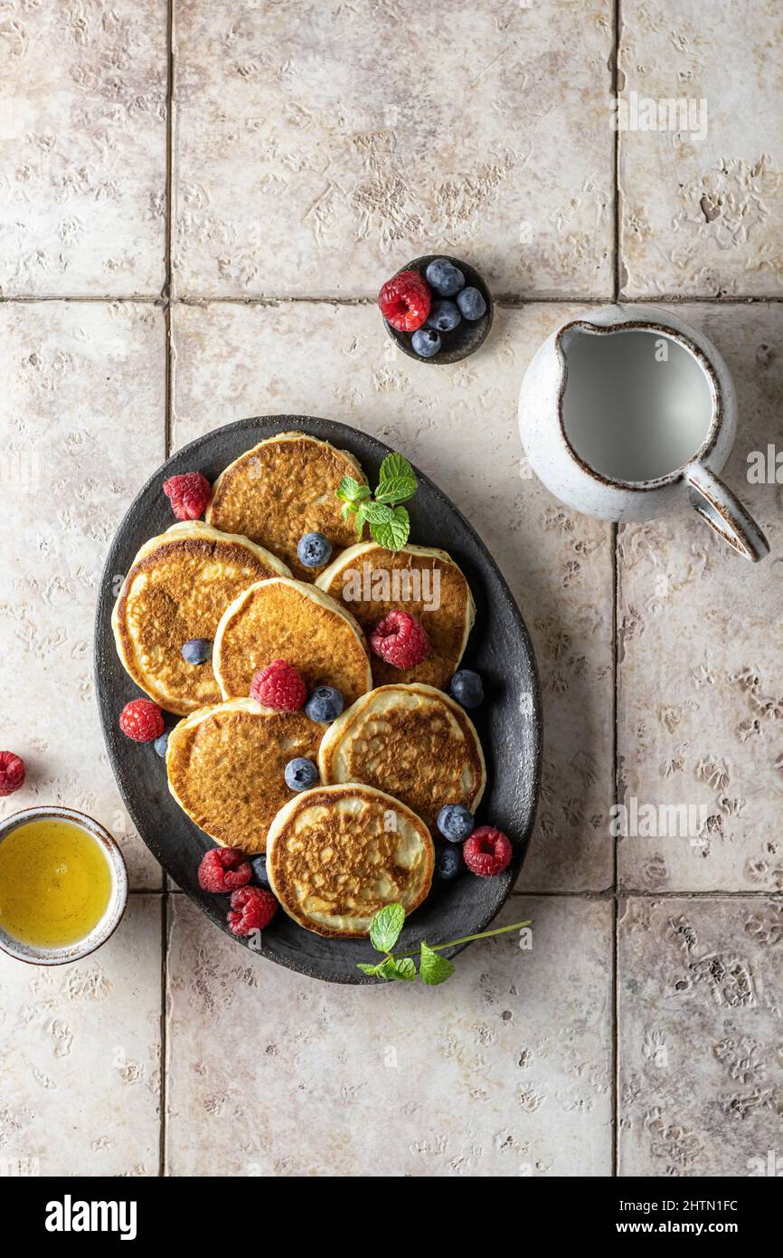 Pancake in piastra di ceramica con lamponi, mirtilli, foglie di menta, miele su sfondo di piastrelle rosa, vista dall'alto Foto Stock