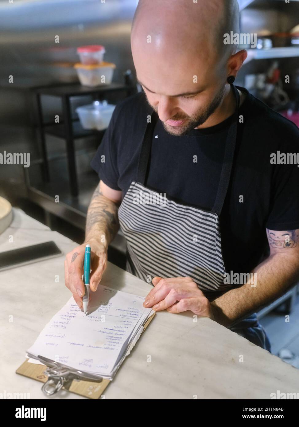 Cuoco controllando l'elenco delle attività per preparare il menu degustazione in un ristorante Foto Stock