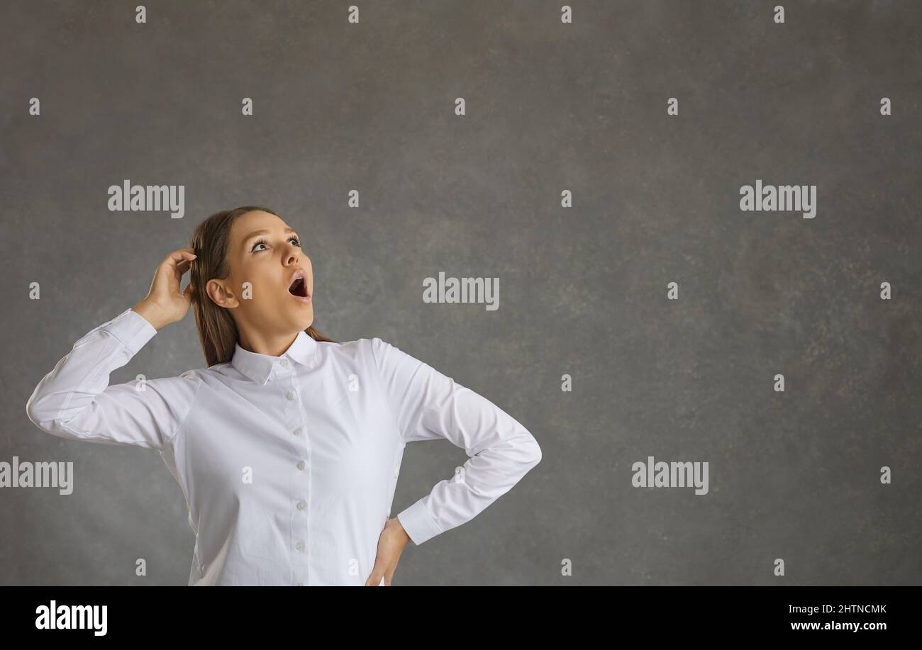 Donna allegra con un'espressione sorpresa guarda in su mentre si alza su uno sfondo grigio. Foto Stock
