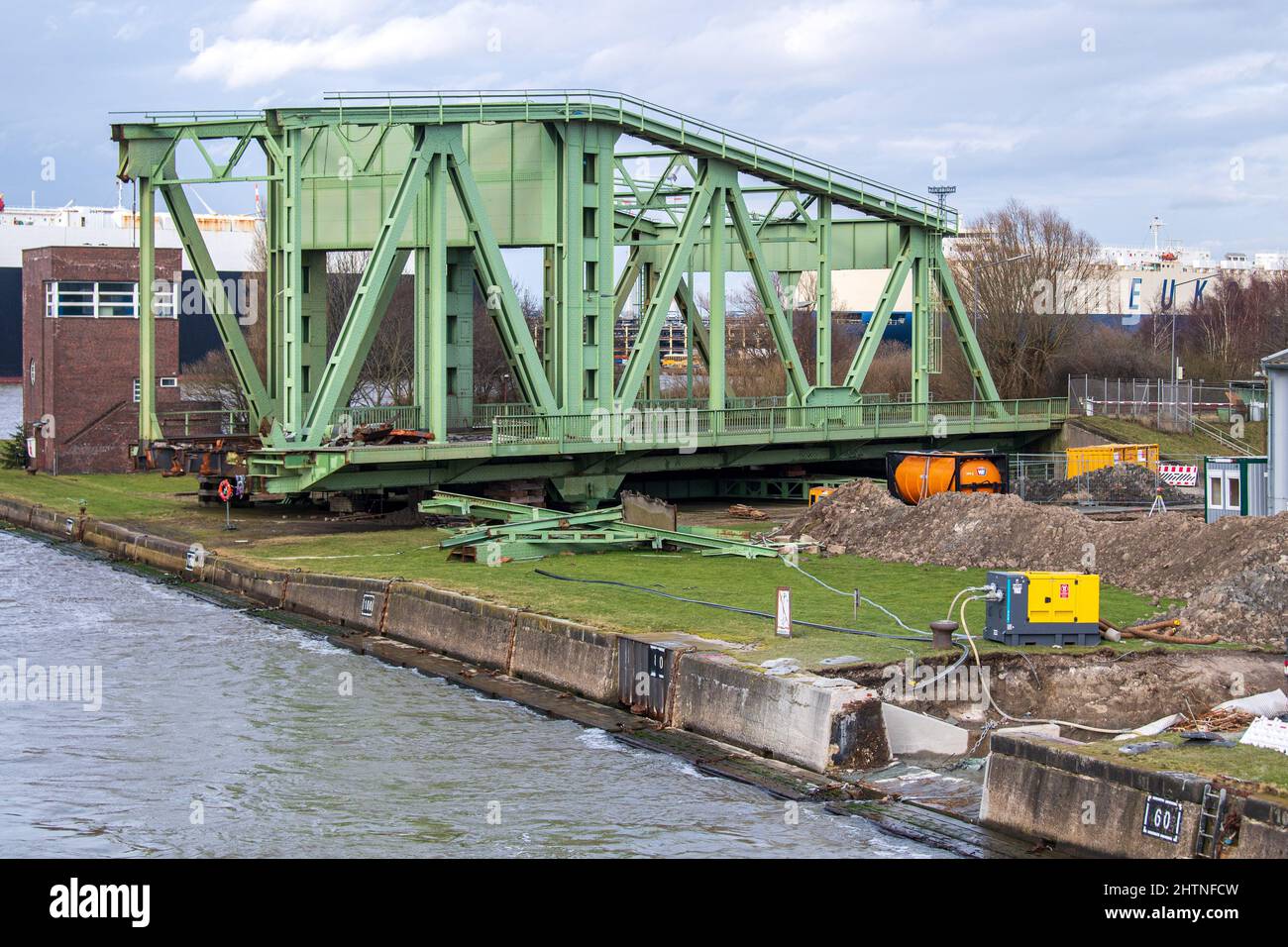 Bremerhaven, Germania. 24th Feb 2022. I lavori di costruzione si stanno svolgendo accanto ai resti del ponte sospeso ferroviario smantellato presso la North Lock nell'area portuale. Una trave in acciaio si era rotta sul ponte sospeso ferroviario di oltre 90 anni fa il 1 aprile 2021, in modo che non funzionava più. È stata tolta dalla sua posizione e ora viene gradualmente smantellata a terra. Quasi un anno dopo l'incidente che ha coinvolto un ponte sospeso ferroviario nel porto di Bremerhaven, sono in corso lavori di costruzione per un servizio di traghetto in sostituzione temporanea. Credit: Sina Schuldt/dpa/Alamy Live News Foto Stock
