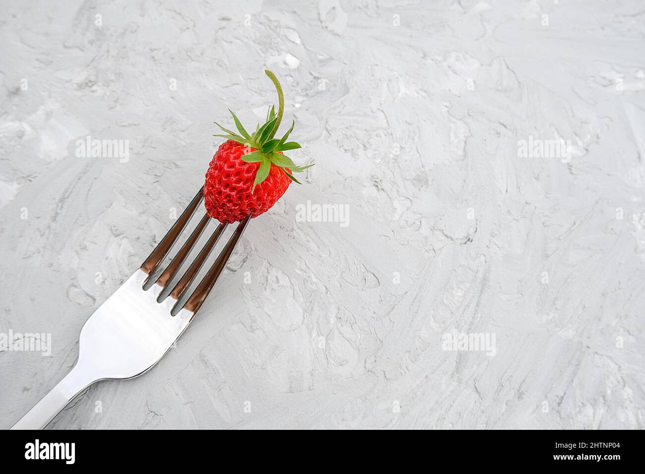 Fragola rossa matura su forchetta su sfondo di tavola in pietra grigia con spazio copia. Concetto di dieta alimentare o vegetarianismo. Vista dall'alto dallo stile minimale. Foto Stock
