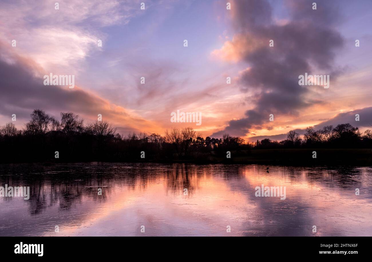 Tramonto sul cielo colorato su un lago ghiacciato. Bulwell Hall Park Nottingham Inghilterra Regno Unito Foto Stock