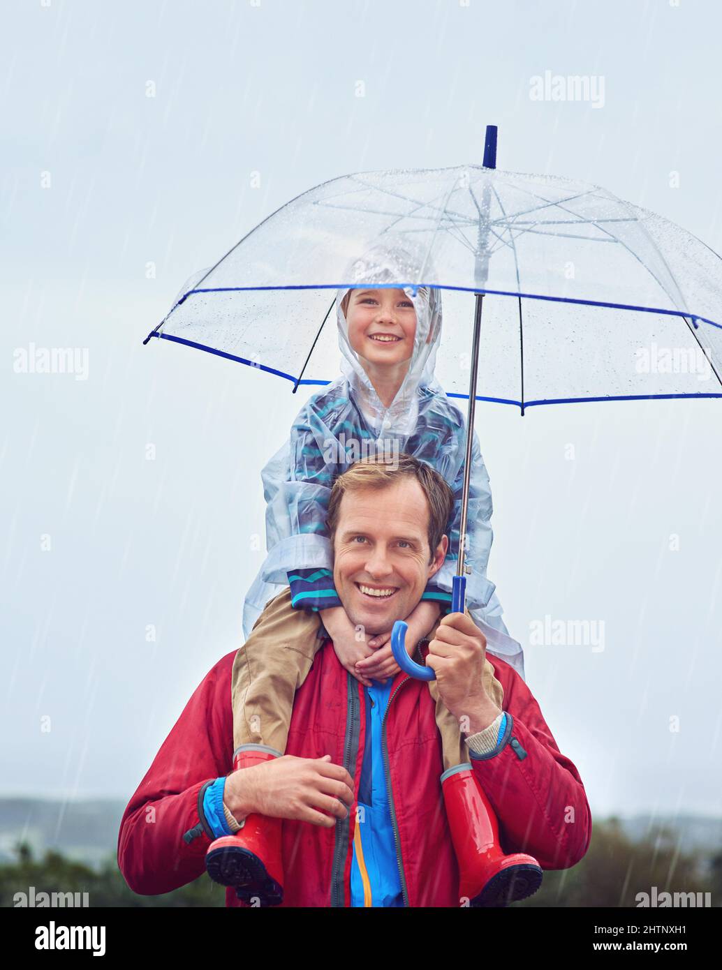 Il tempo non si levano in piedi nel nostro senso. Ritratto corto di un padre che porta il figlio sulle spalle fuori sotto la pioggia. Foto Stock