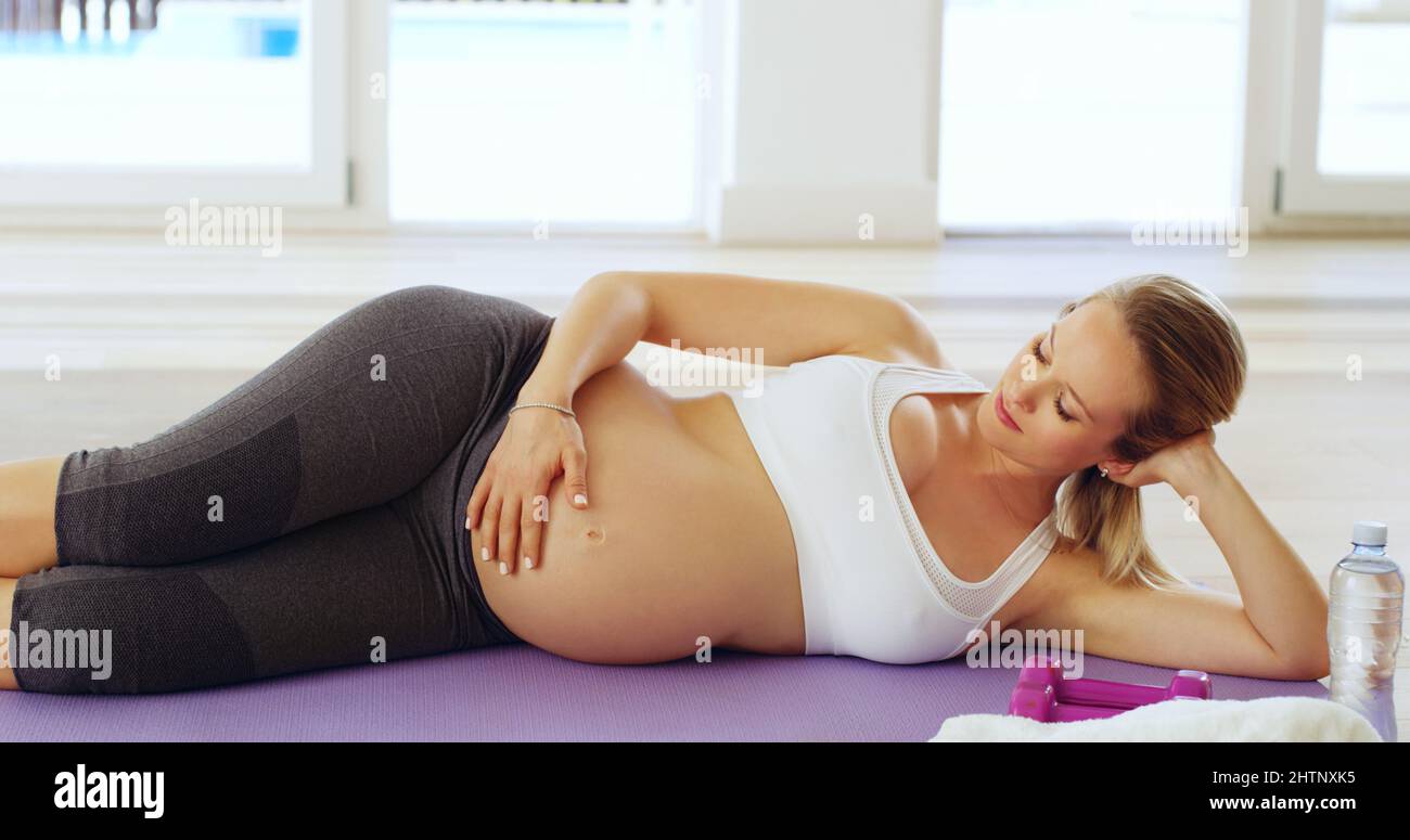 Mamma non può aspettare di incontrarti. Scatto corto di una giovane donna incinta attraente che si trova sul suo lato su un tappeto yoga. Foto Stock