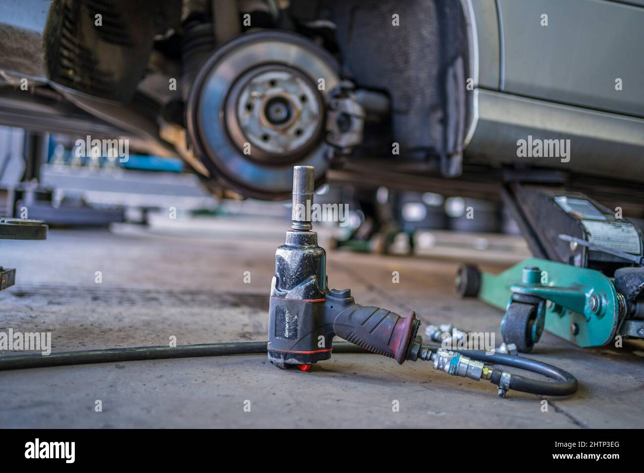 Un'auto sollevata su un martinetto in un garage con la ruota rimossa e una chiave a percussione pneumatica in primo piano. Foto Stock