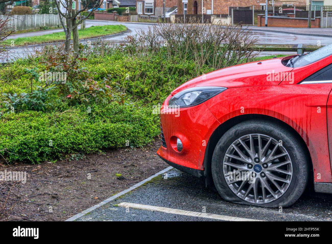 Una vettura Ford rossa parcheggiata con uno pneumatico anteriore lato sinistro piatto. Foto Stock