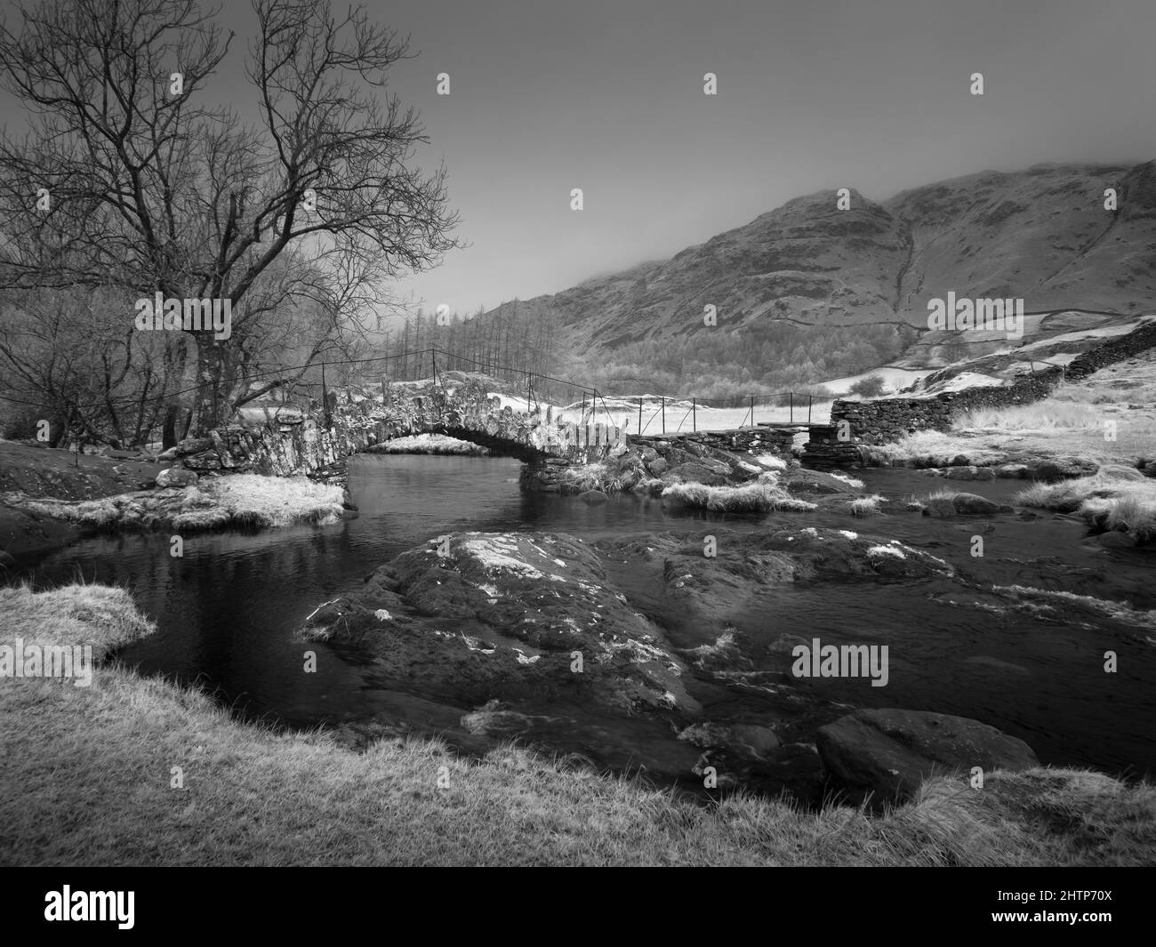 Un'immagine infrarossa di Slater Bridge, il ponte pedonale del 17th secolo sopra il fiume Brathay sotto Lingmoor cadde a Little Langdale nel Parco Nazionale del Distretto dei Laghi Inglese, Cumbria, Inghilterra. Foto Stock
