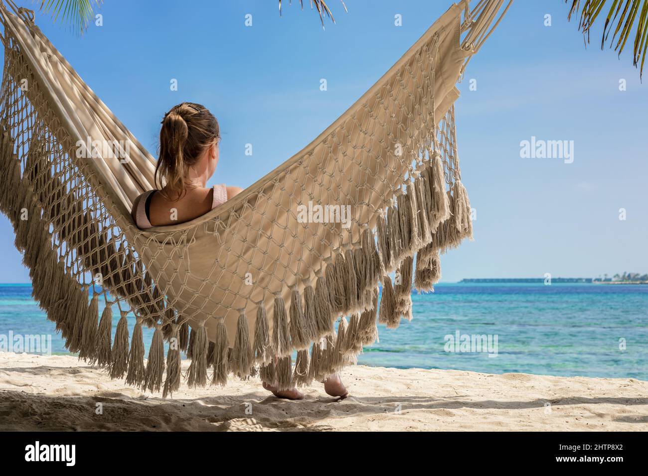 Vacanze in spiaggia con donna rilassante in amaca tra palme da cocco, sabbia bianca, cielo blu e acqua turchese. Resort panoramico isola di ma Foto Stock