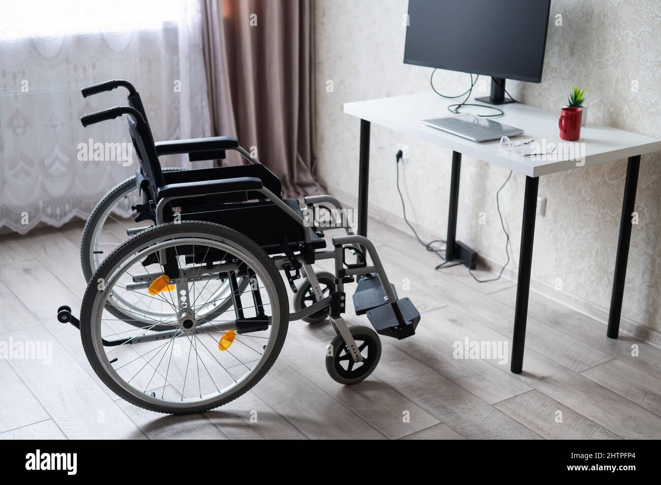 Luogo di lavoro per una persona con disabilità. Sedia a rotelle al tavolo con un computer. Foto Stock