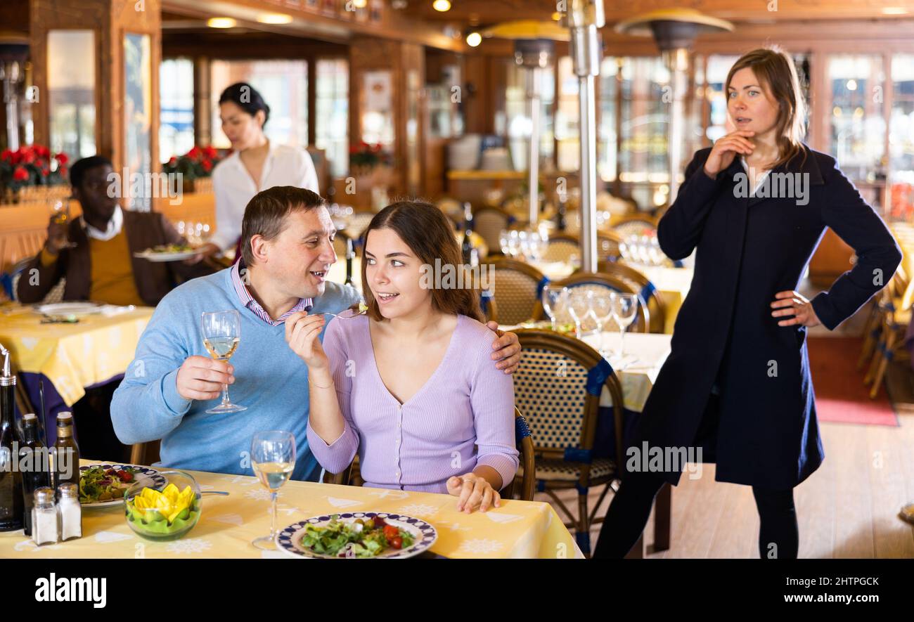 Donna stupita guardando il marito che mangiava con la sua padrona Foto Stock
