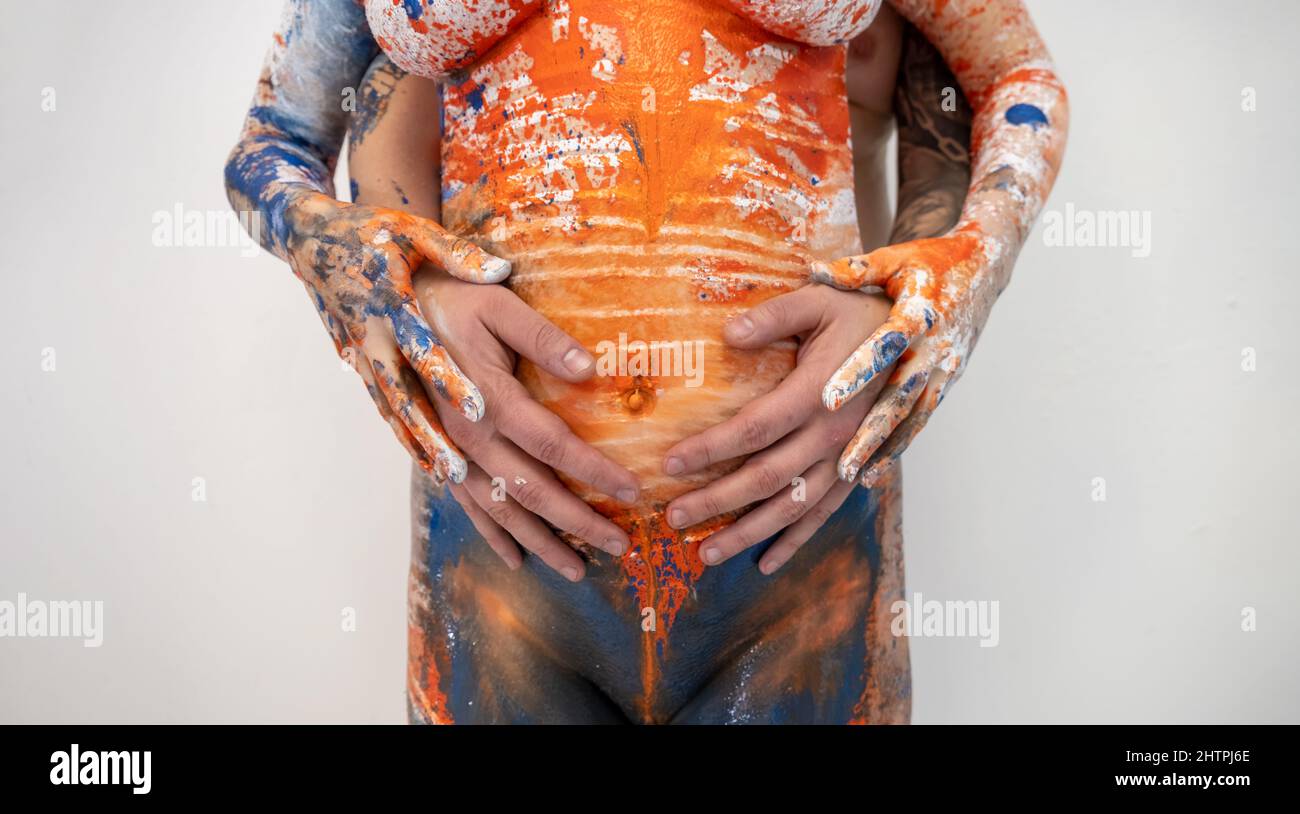 mani di bel giovane uomo, marito, abbraccio, toccando ventre nudo di bel arancio incinta, bianco, donna rossa dipinta blu, moglie, da dietro Foto Stock
